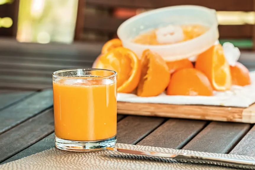 Verre de jus d’orange frais posé sur une table en bois, devant des oranges coupées et un presse-agrumes